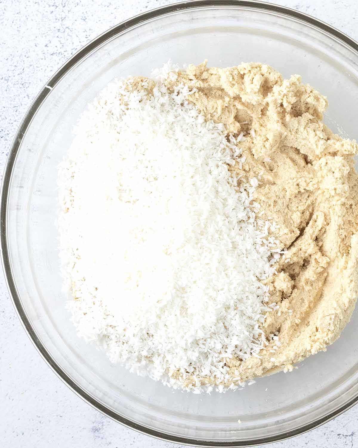 Coconut cookie dough with shredded coconut on top waiting to be mixed in.