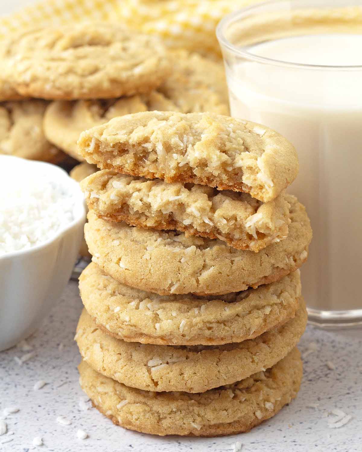 A stack of five coconut cookies, the one on top has been split in two to show the soft, chewy inner texture.