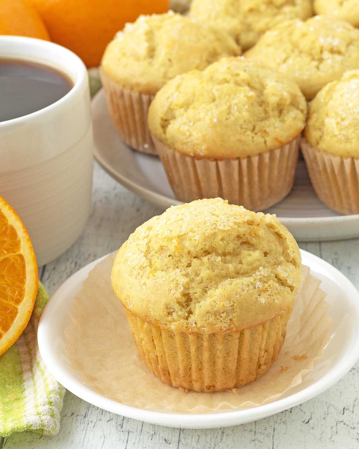 An orange muffin on a plate, the muffin wrapper has been peeled away.