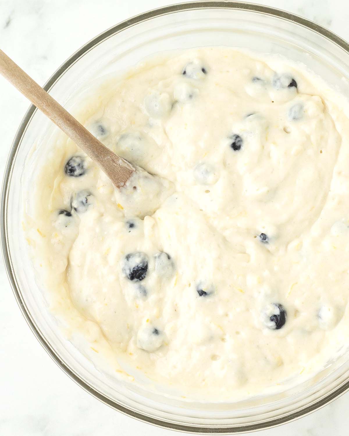 Mixed vegan lemon blueberry muffin batter in a glass bowl.