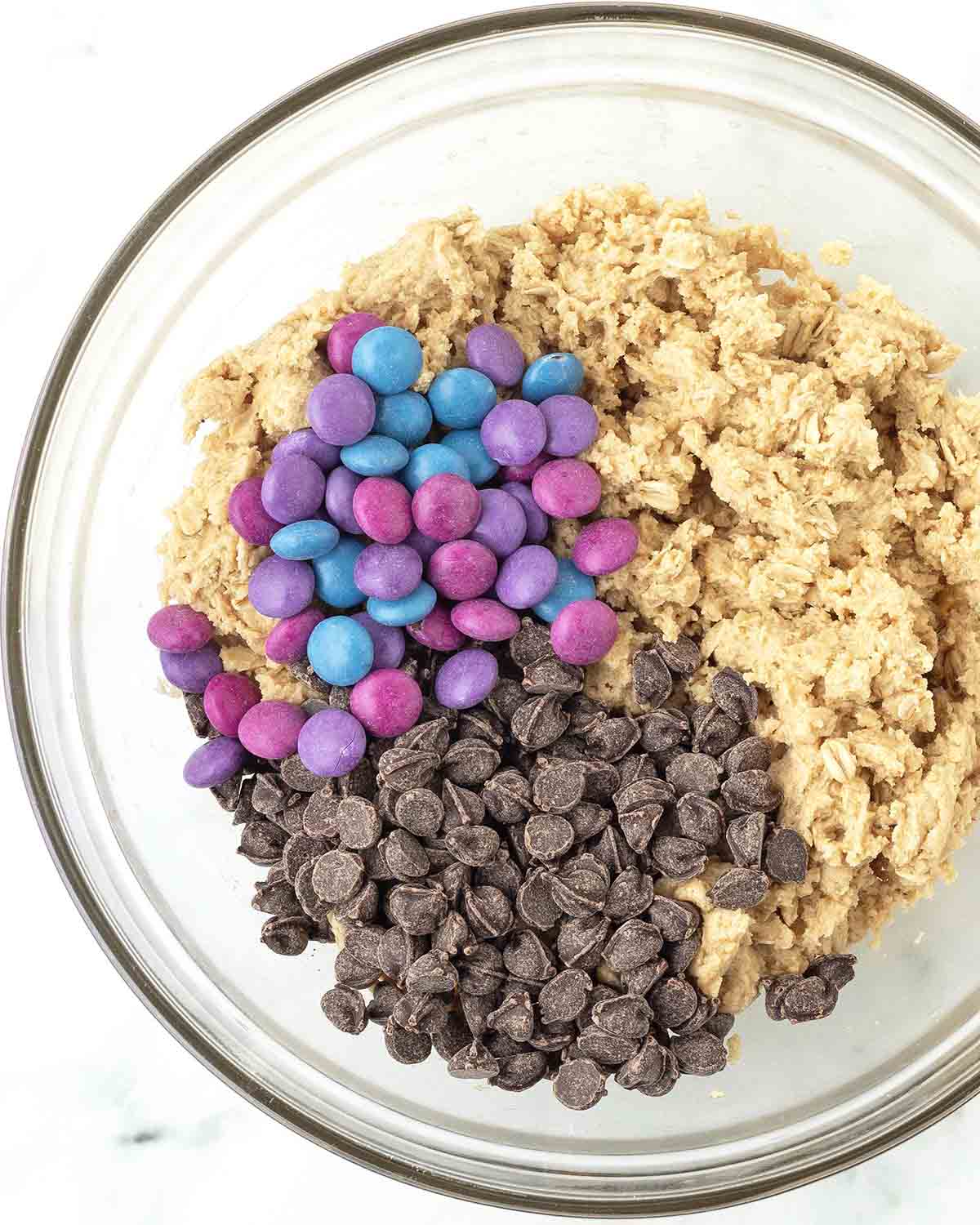 Monster cookie dough with chocolate candies and chocolate chips on top waiting to be mixed in.