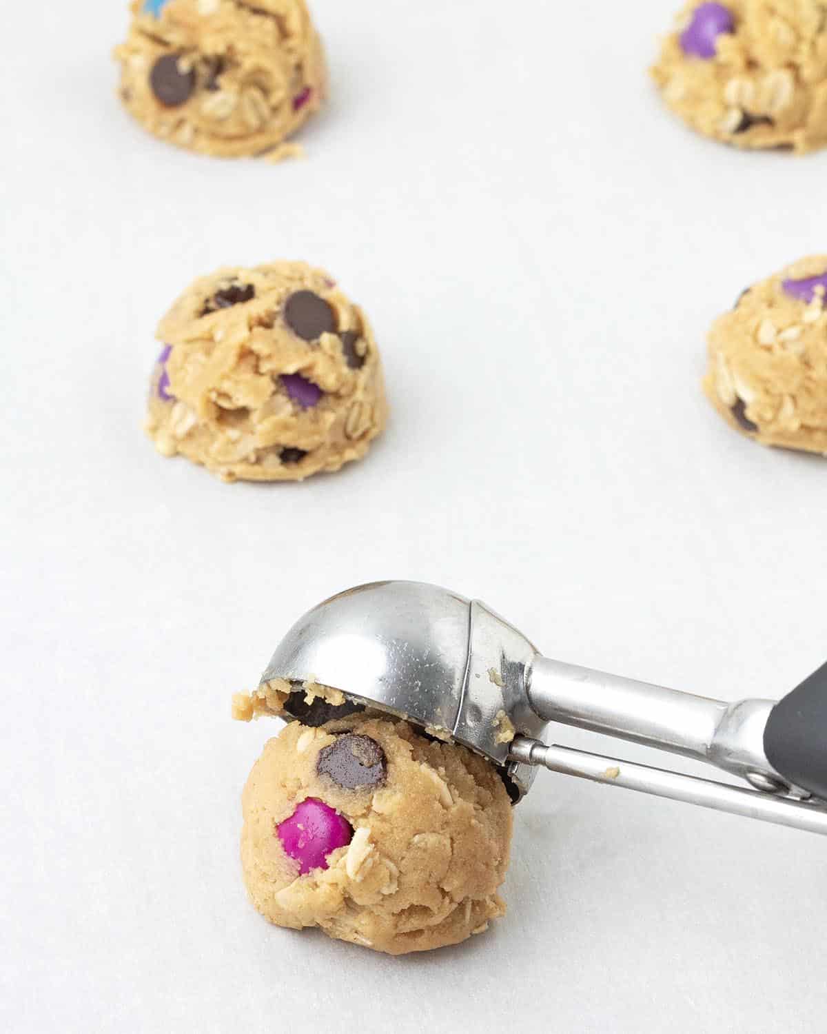 A cookie scoop scooping unbaked monster cookie dough onto a parchment lined cookie sheet.