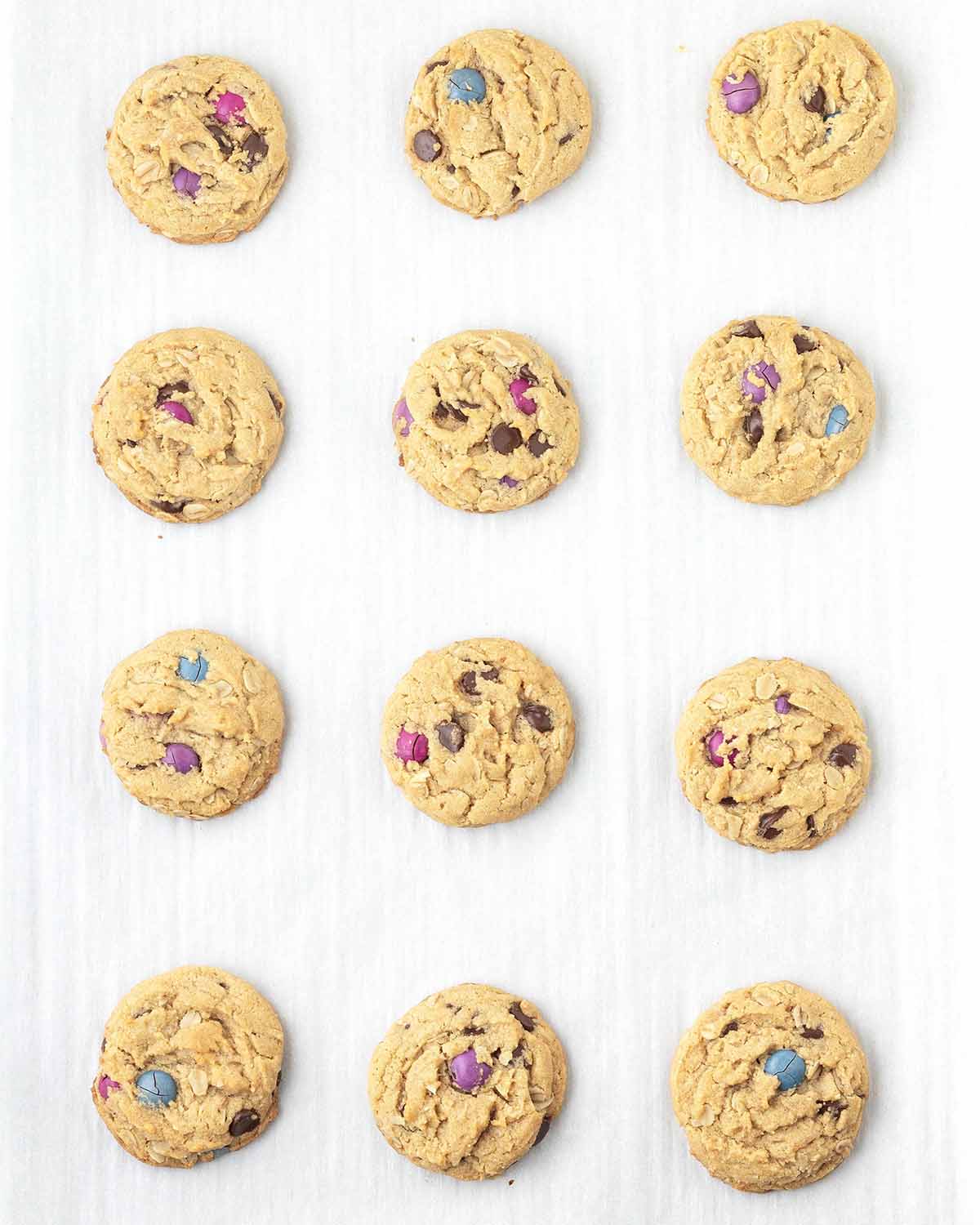 Freshly baked vegan monster cookies on a parchment lined cookie sheet.