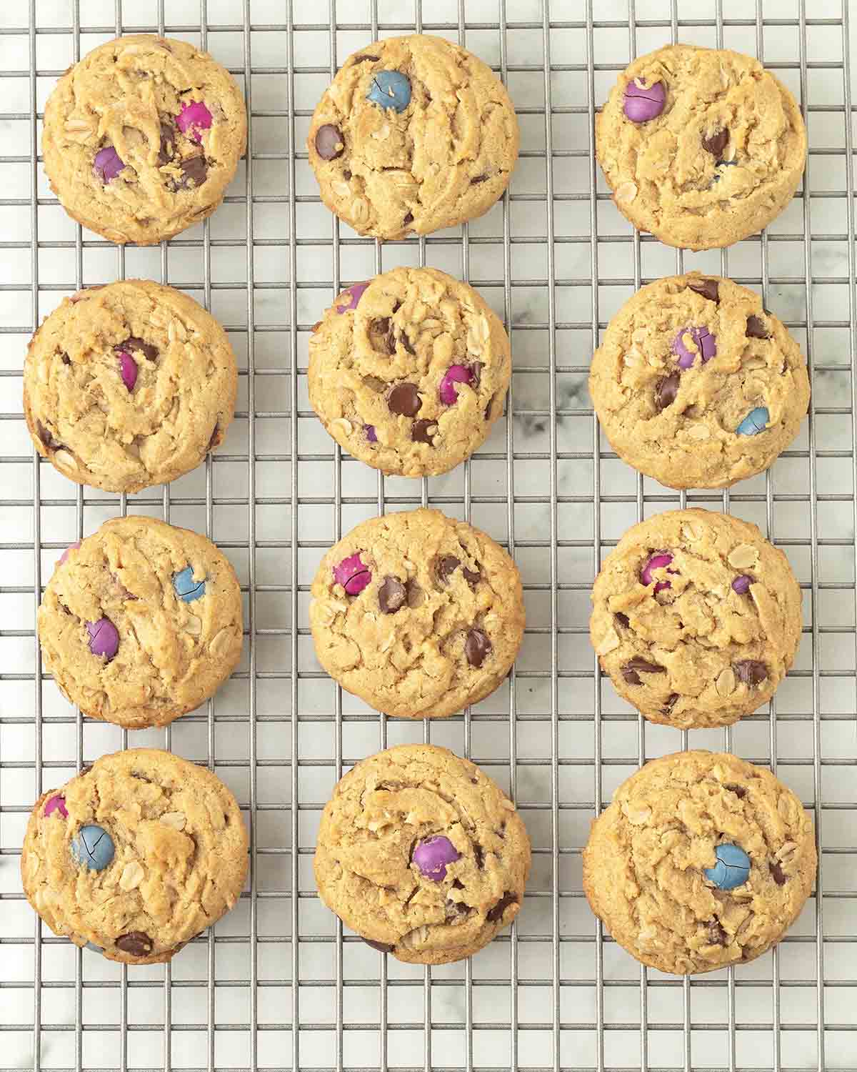 Monster cookies sitting on a metal cooling rack.