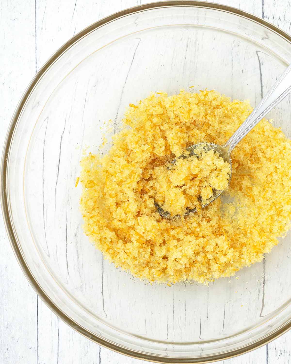 Orange zest, sugar and a spoon in a glass bowl.