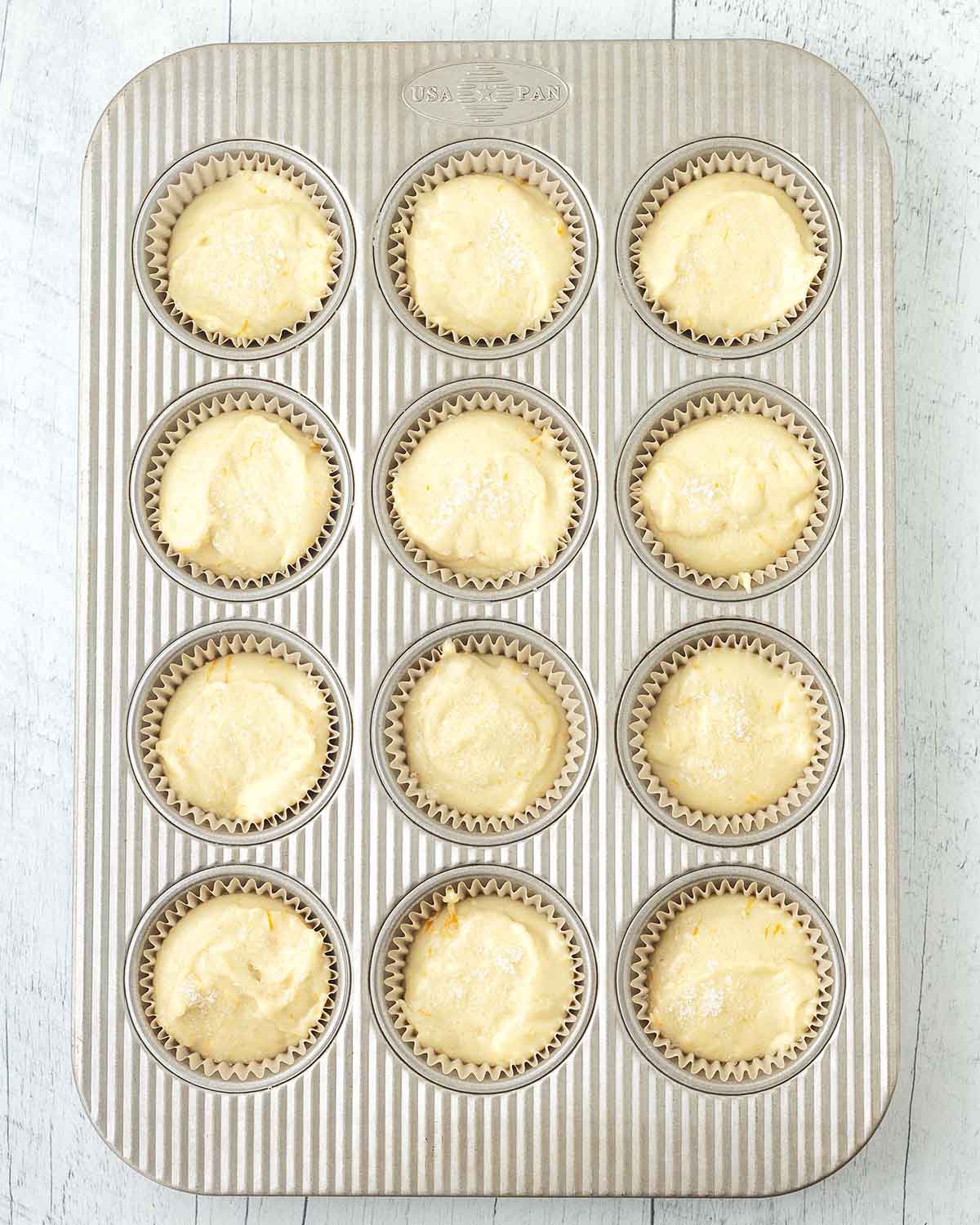 Unbaked orange muffins in a muffin pan.