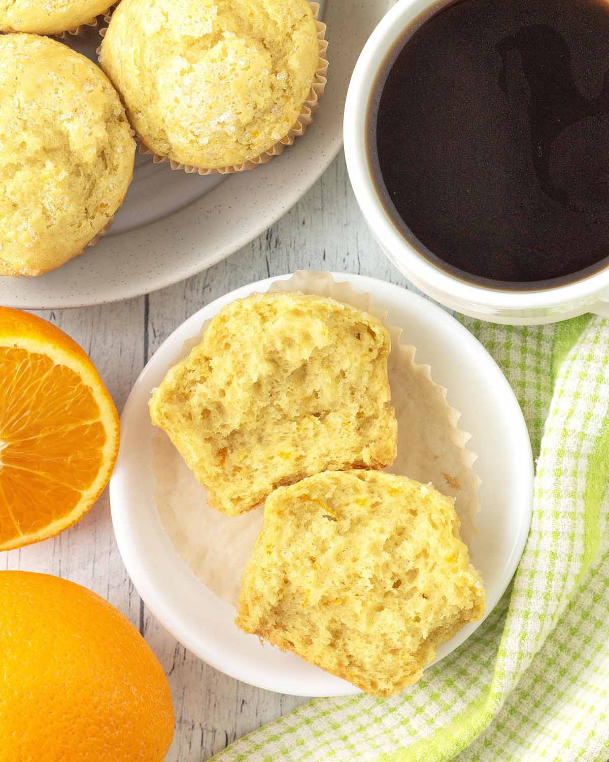 An orange muffin on a small plate, the muffin has been split in half to show the fluffy interior.