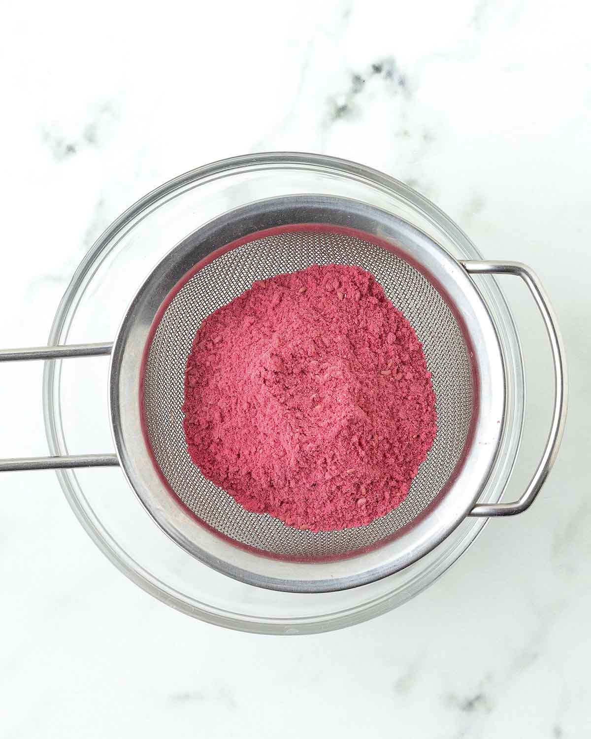 Freeze-dried raspberry powder in a sieve being held over a bowl.