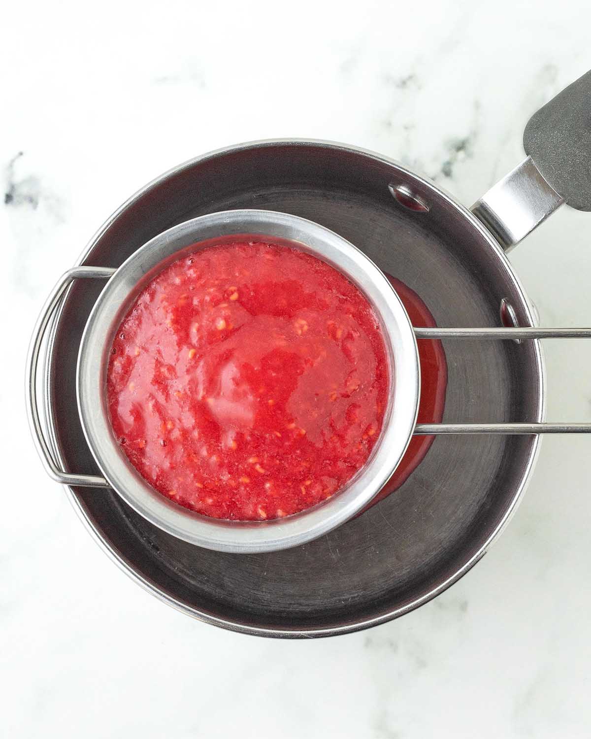 Pureed fresh raspberries in a sieve being held over a pot.