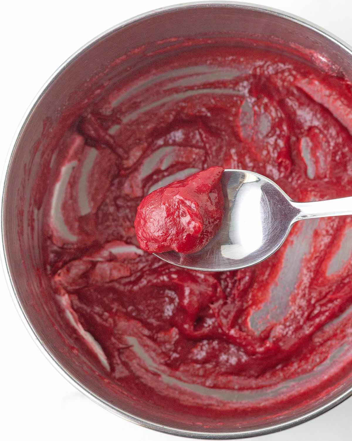 Reduced raspberry puree in a spoon being held over the pot it was made in.