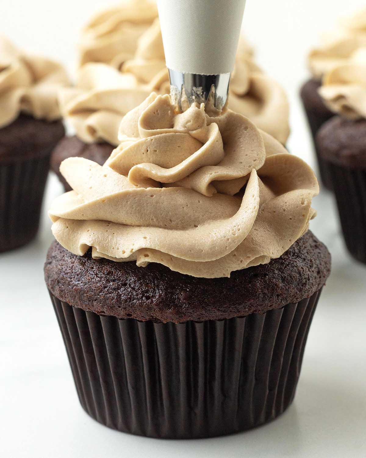 Frosting being piped onto a chocolate cupcake with a white coloured piping bag.