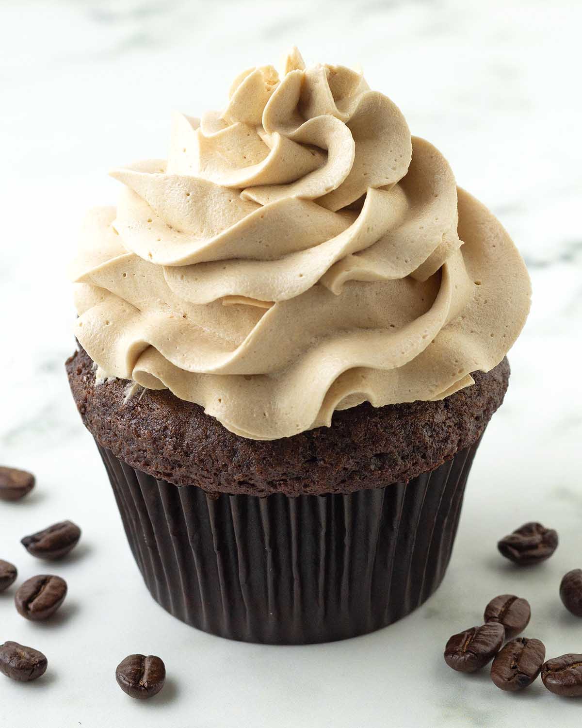 A chocolate cupcake topped with coffee frosting, coffee beans sit on both sides of the cupcake.