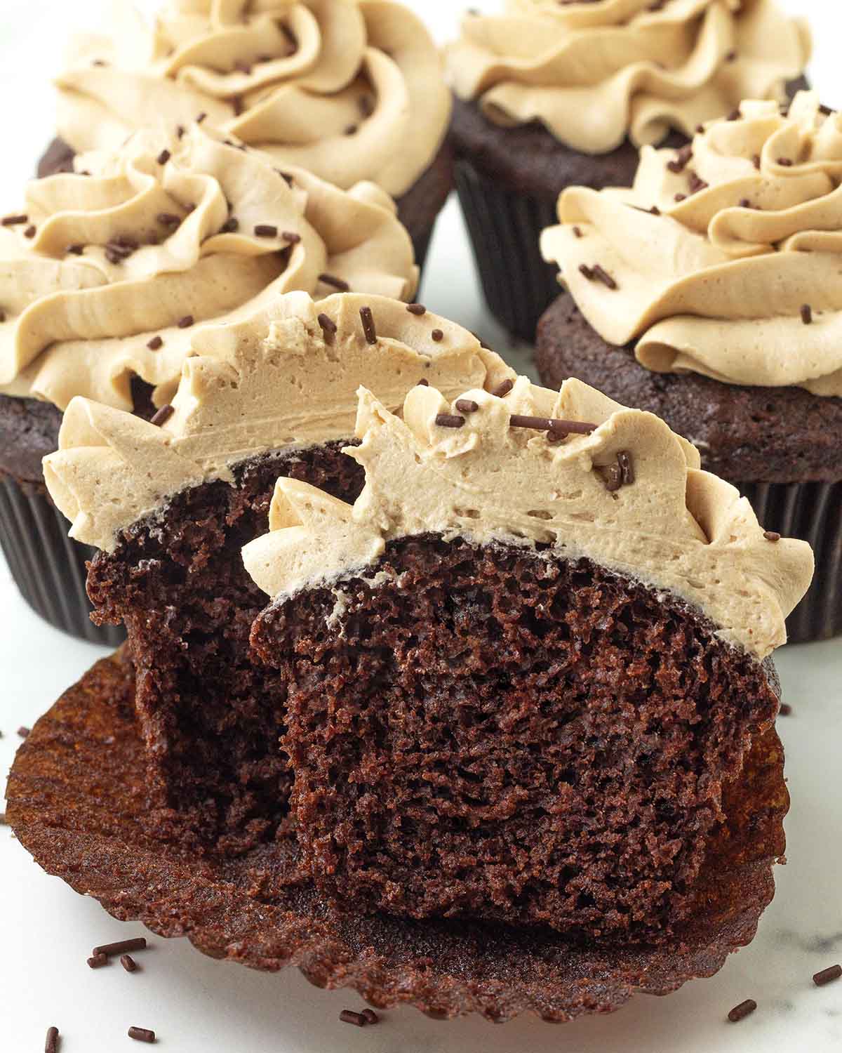 A chocolate cupcake on its peeled away wrapper split in half to show the fluffy interior.