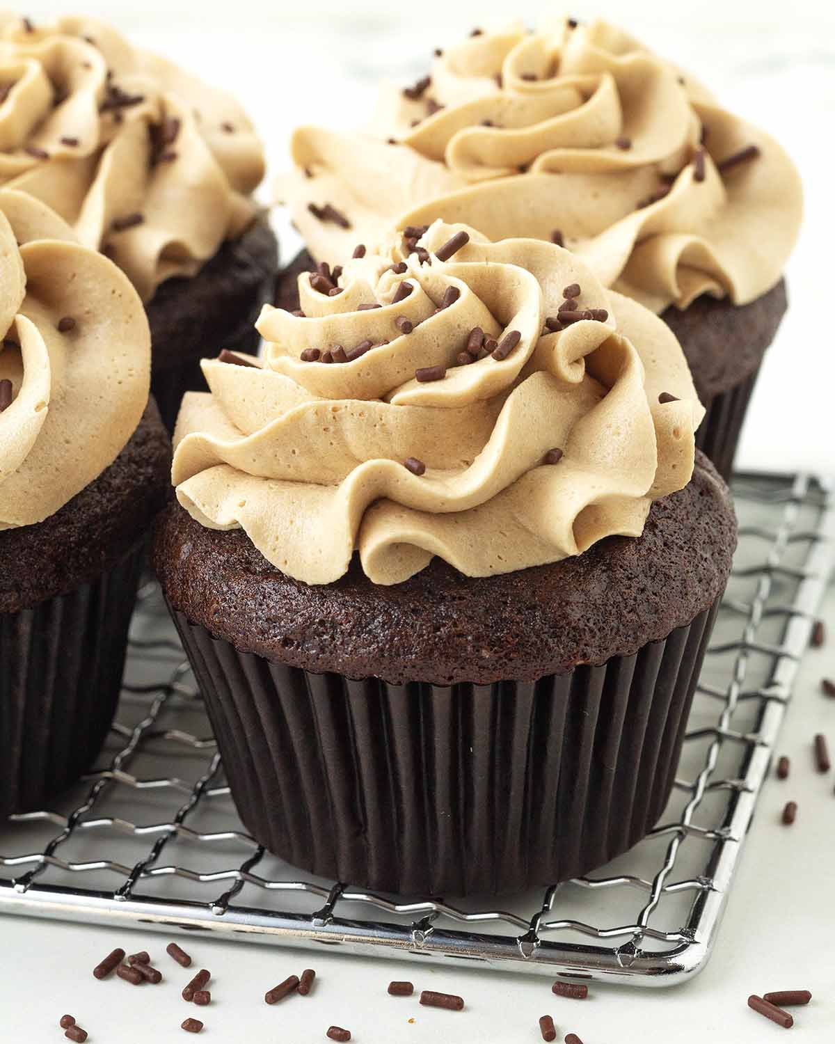 Frosted vegan chocolate cupcakes on a metal rack.