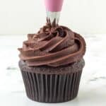 Vegan ganache frosting being piped onto a chocolate cupcake.