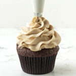 Vegan coffee buttercream frosting being piped onto a chocolate cupcake.