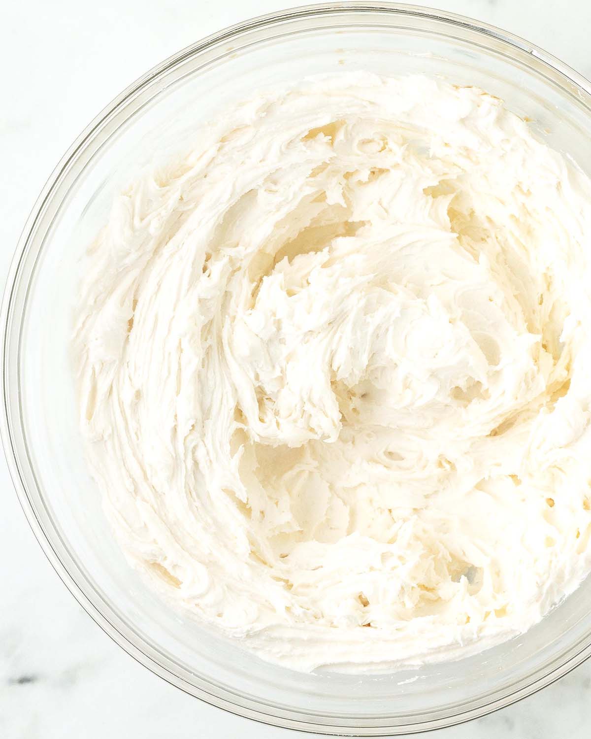 A glass bowl filled with whipped buttercream frosting.