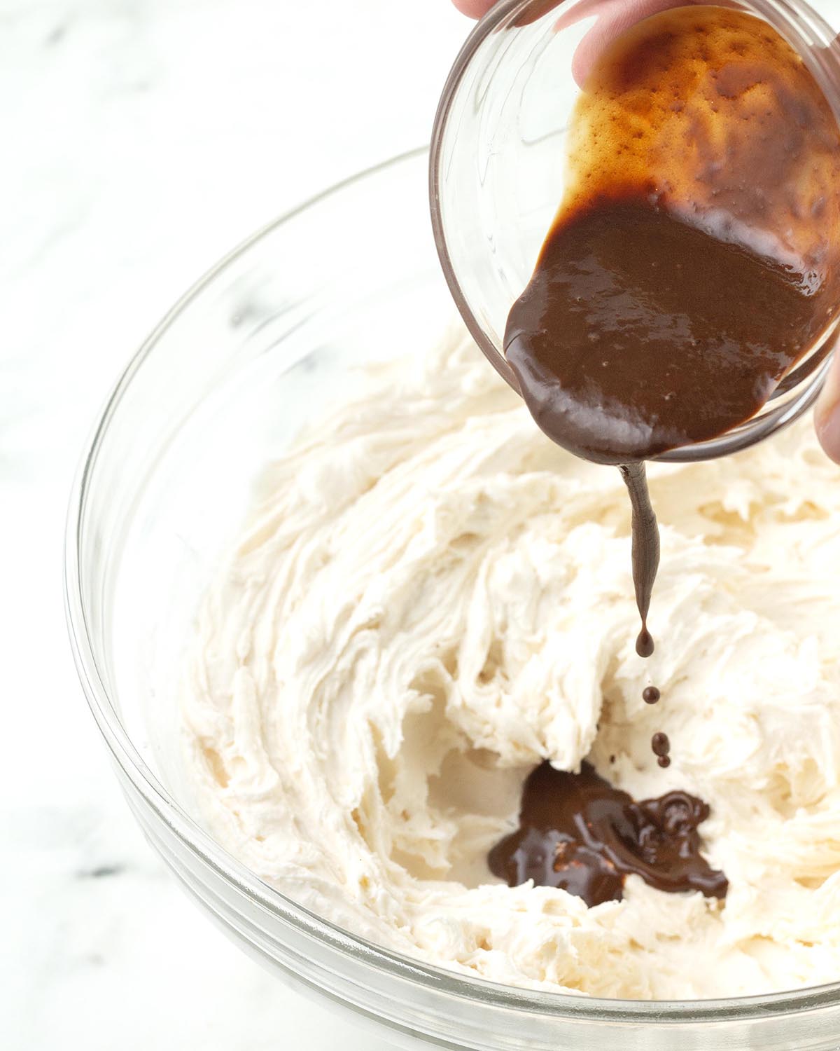 Coffee mixture being poured into a bowl of whipped buttercream.