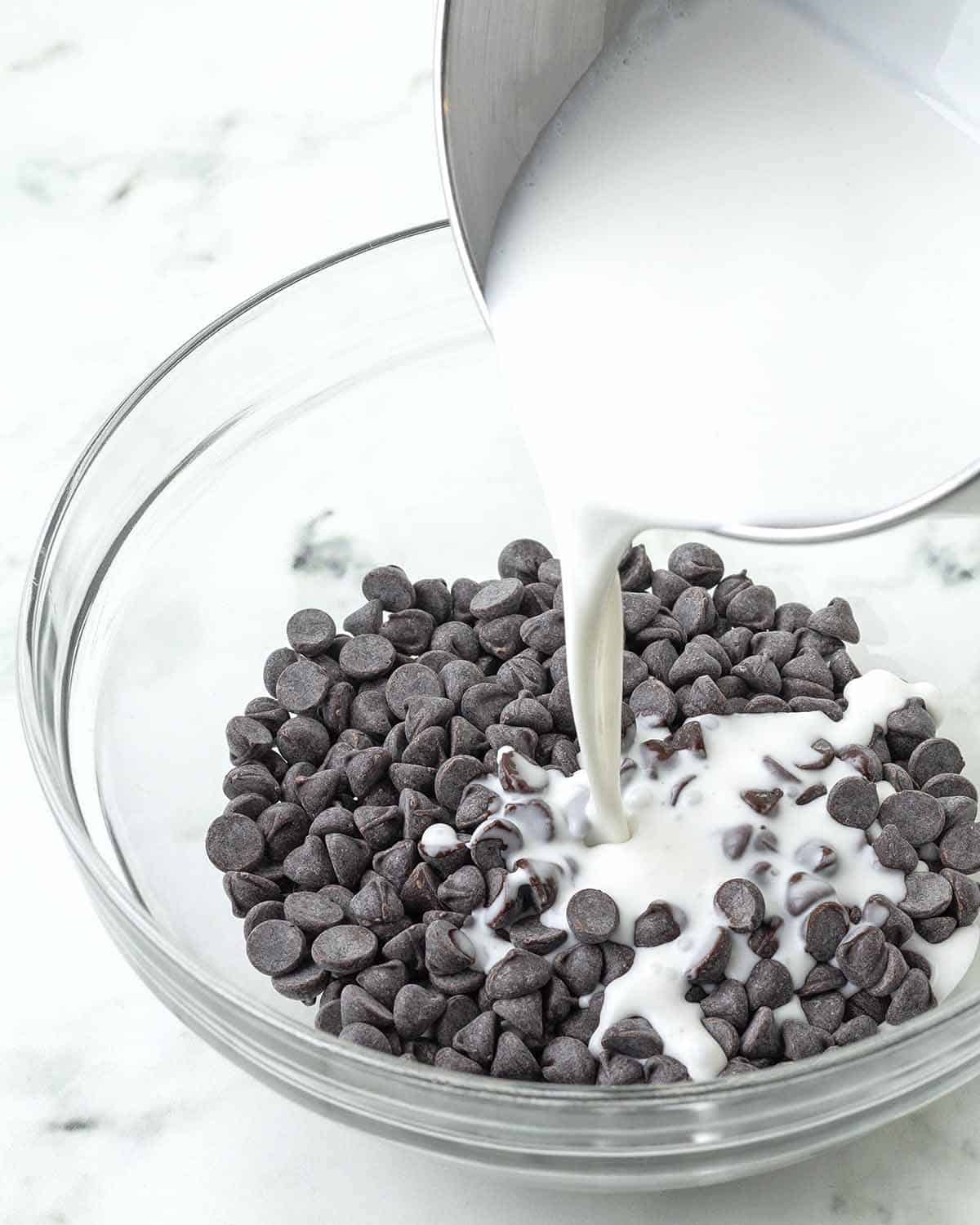 Warmed vegan heavy cream being poured from a pot into a bowl of chocolate chips.