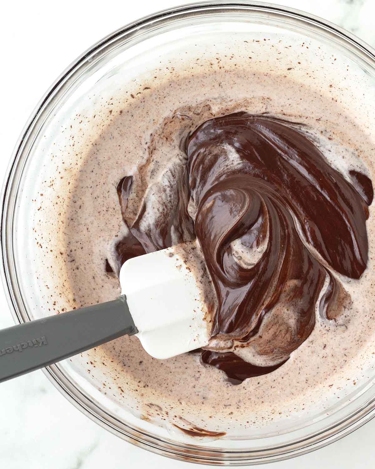 A rubber spatula mixing chocolate and heavy cream in a glass bowl.