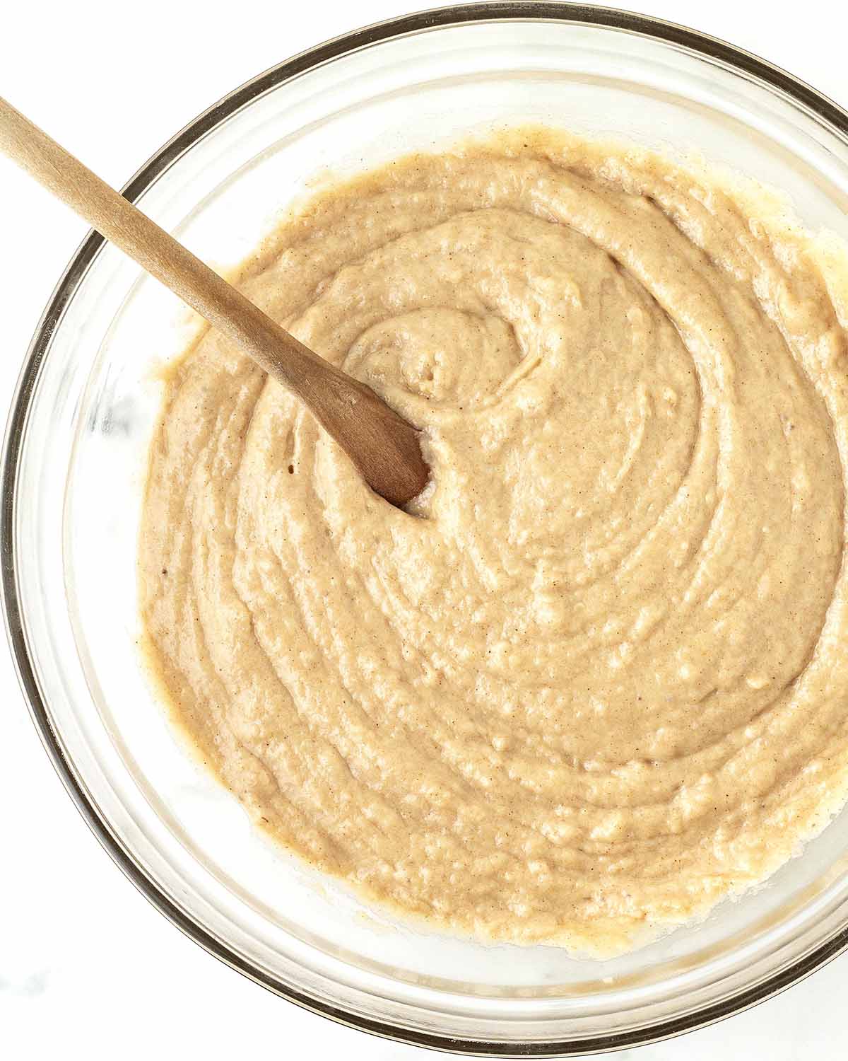 Mixed banana bread batter and a wooden spoon in a glass mixing bowl.