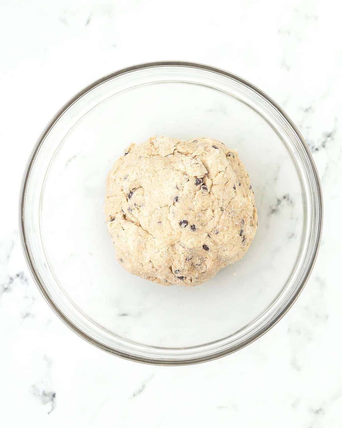 A ball of vegan chocolate chip scone dough in a glass bowl.