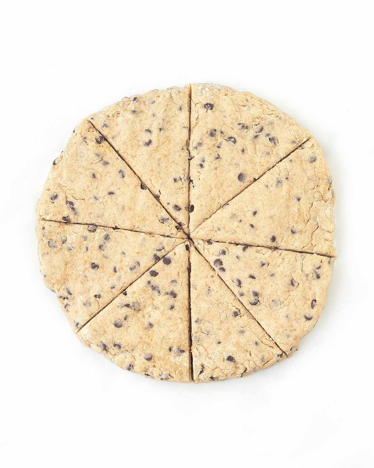 A round disc of chocolate chip scone dough that has been cut into eight wedges.