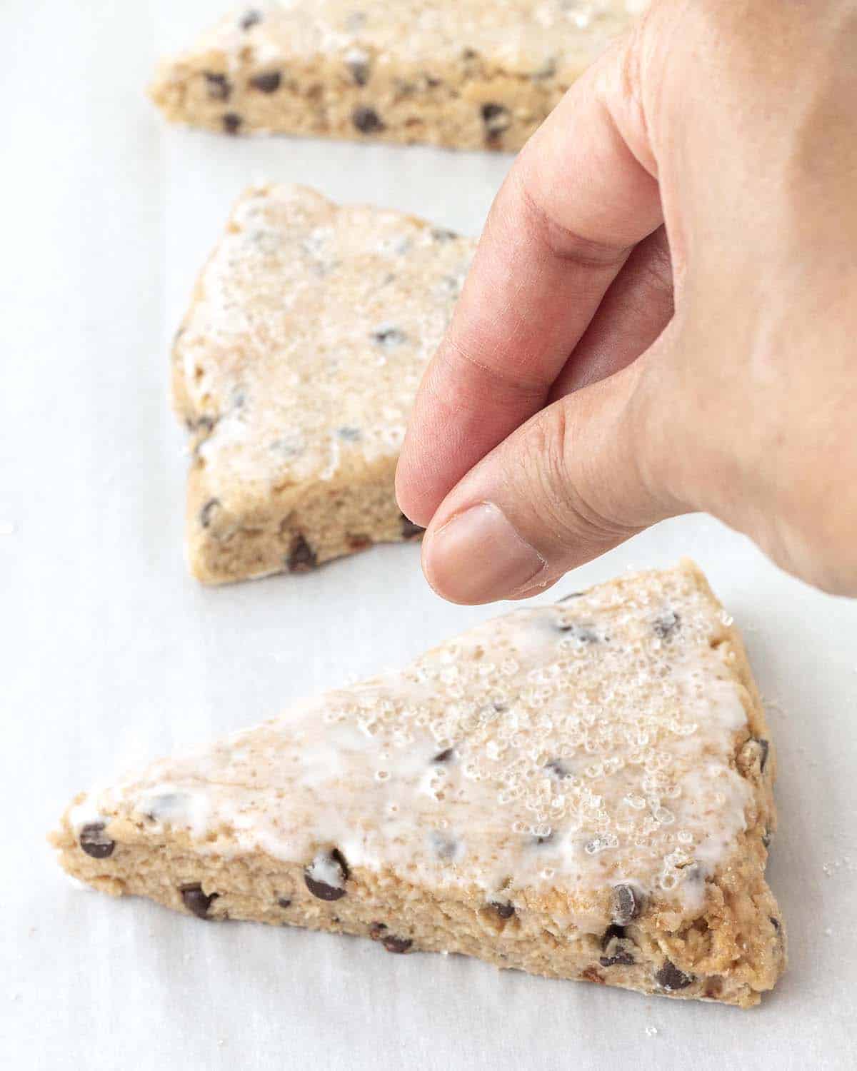 A hand sprinkling coarse sugar on top of an unbaked chocolate chip scone.