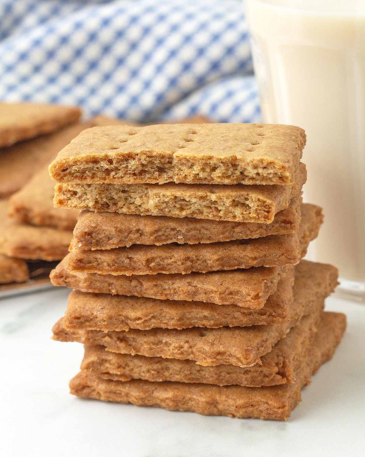 A stack of graham crackers, the one on top has been split in two to show the crisp inner texture.