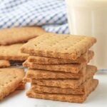 A stack of vegan graham crackers, a glass of milk and more crackers sit in the background.