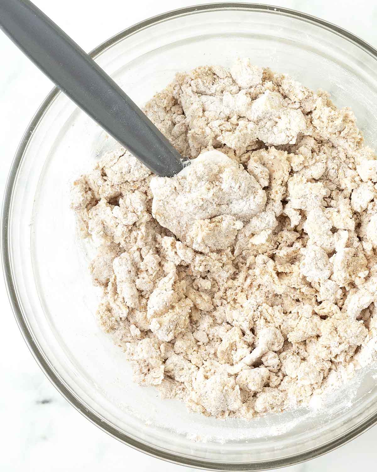 Dough for vegan graham crackers being mixed with a spatula in a glass bowl.