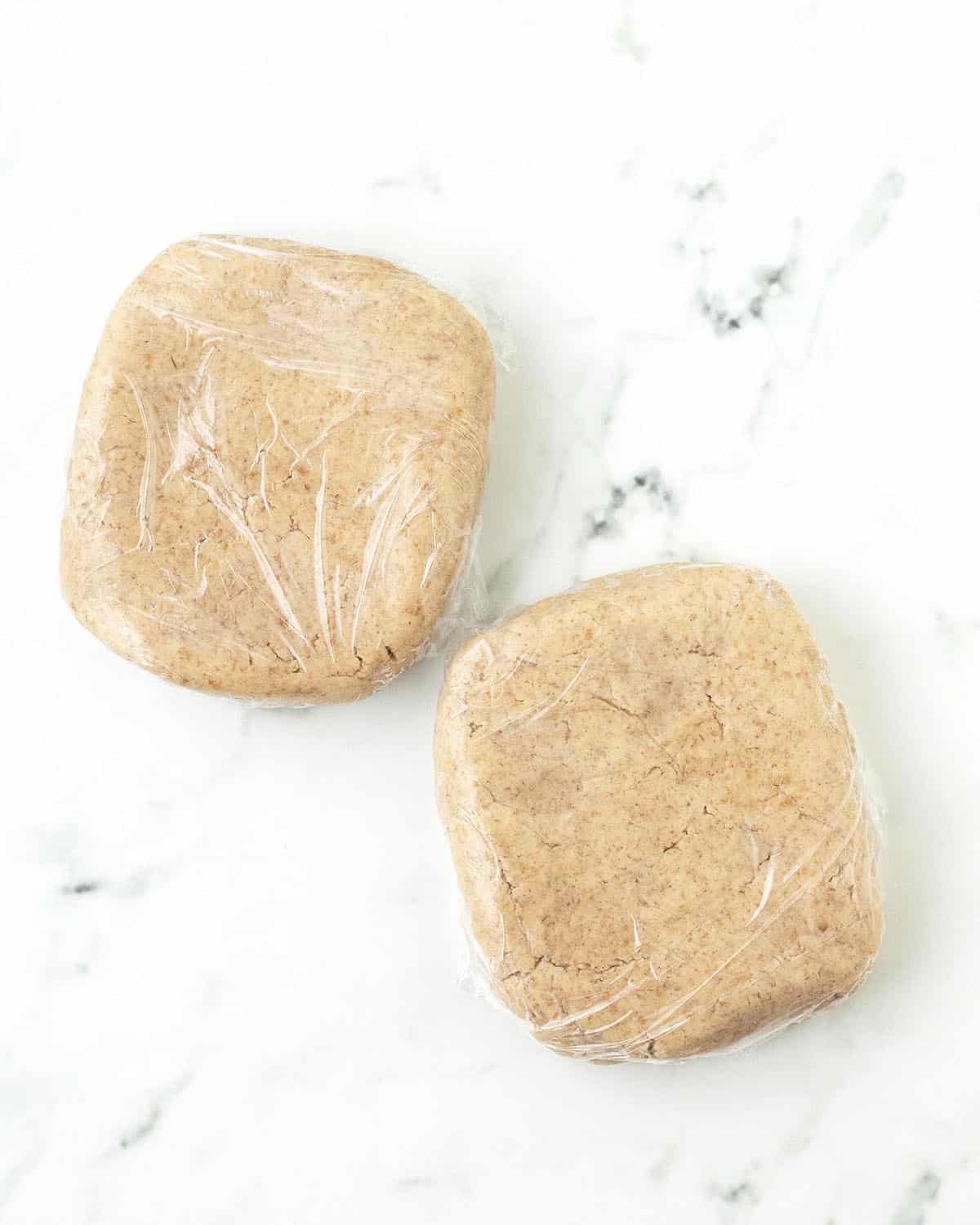 Two pieces of cookie dough wrapped in plastic wrap.