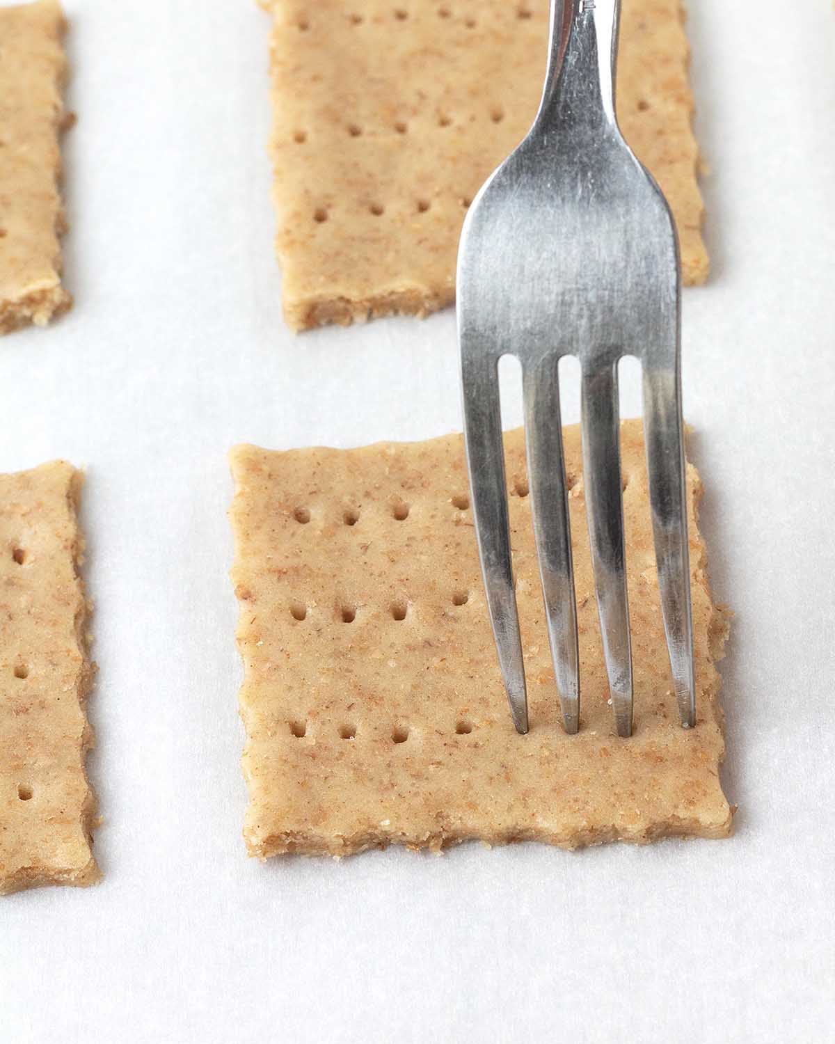 A fork pressing holes into an unbaked graham cracker.