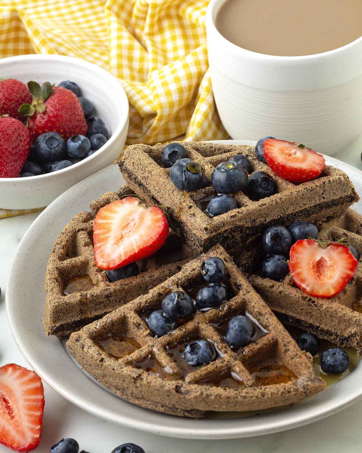 A waffle on a white plate, maple syrup and fresh berries top the waffle.