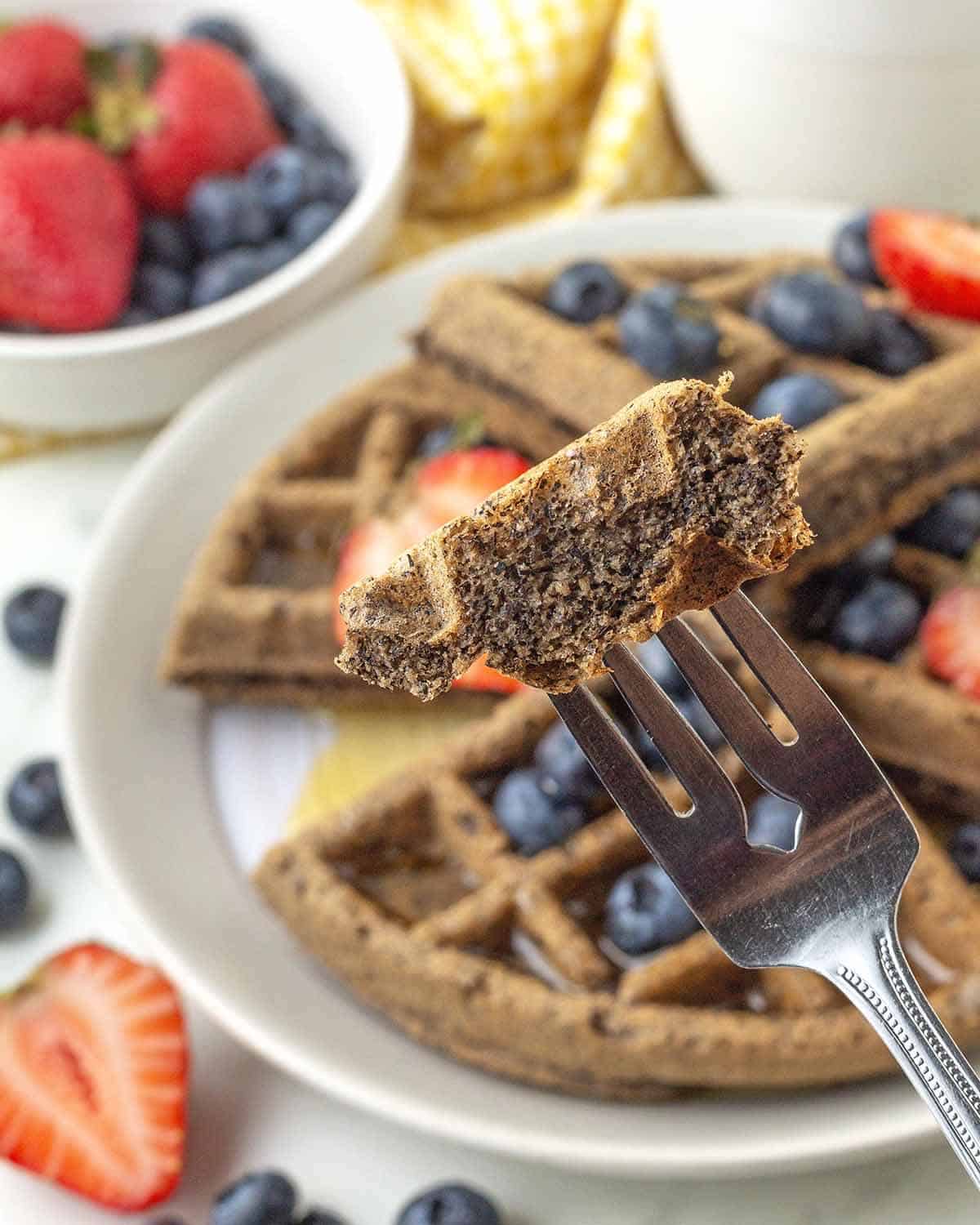 A fork holding up a piece of a buckwheat waffle to show the fluffy inside.