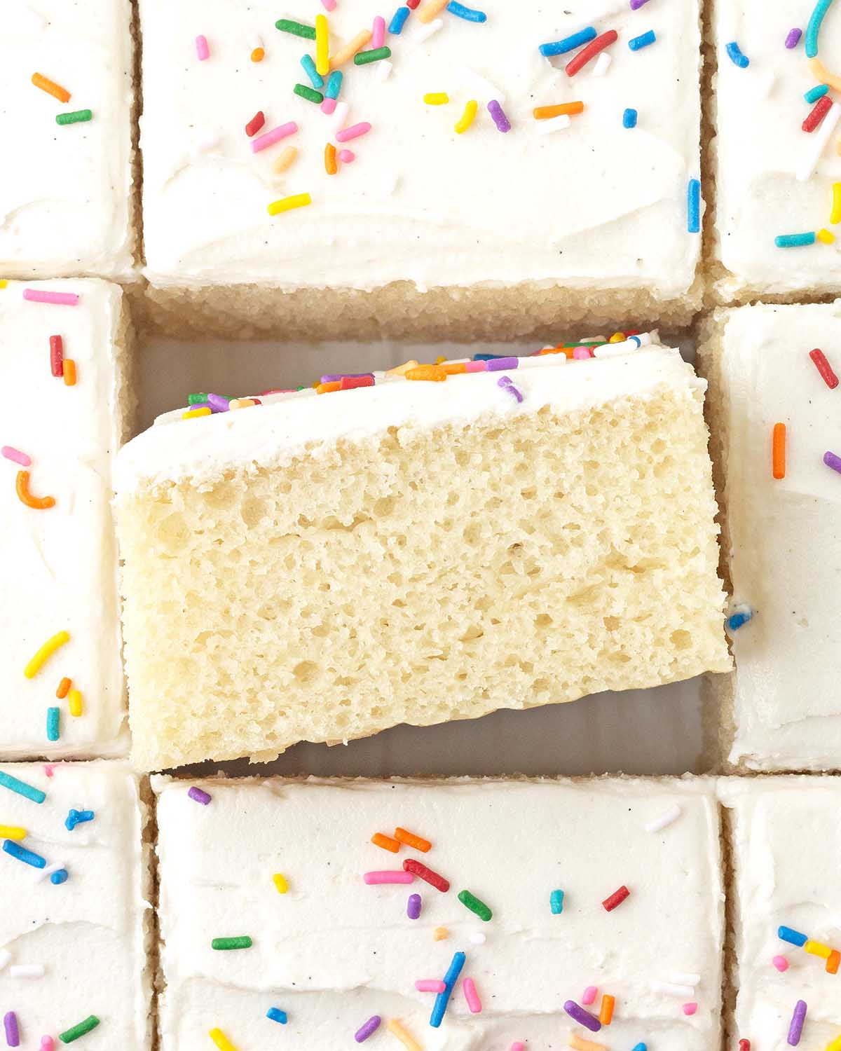 An overhead image of sliced vanilla sheet cake, the square in the middle is on its side to show the fluffy texture.