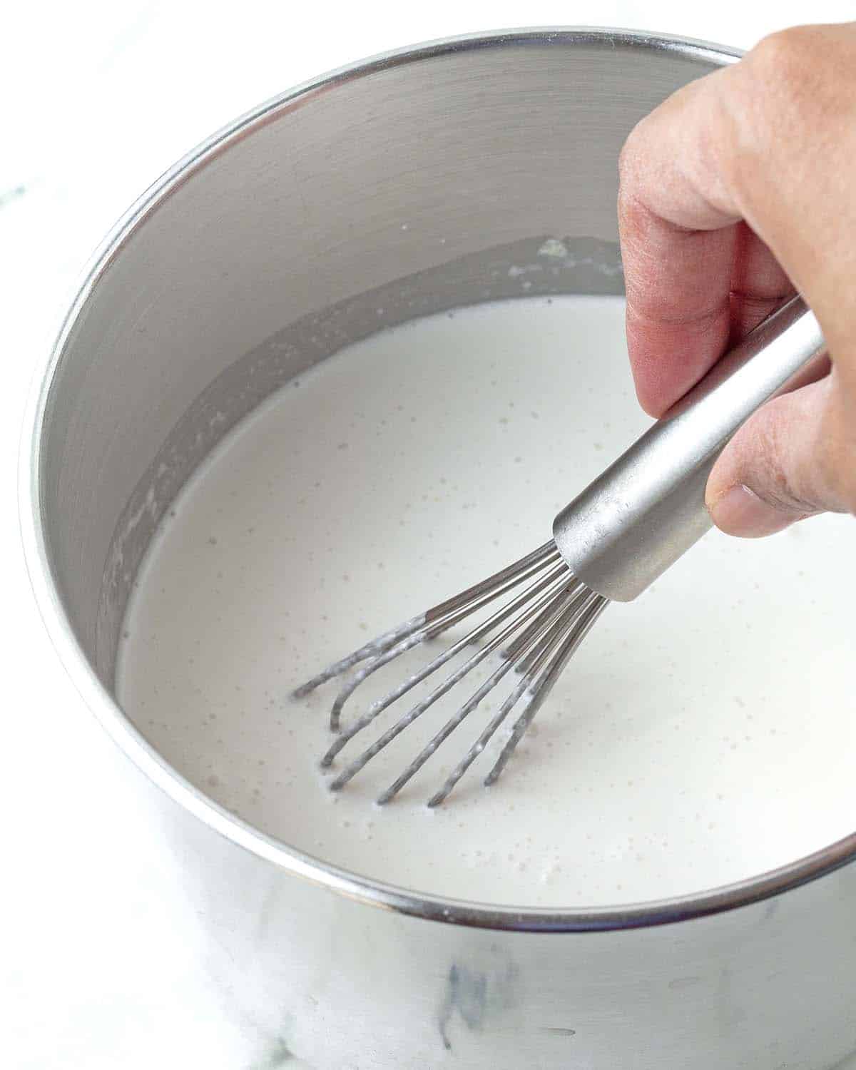 A hand whisking custard in a pot.
