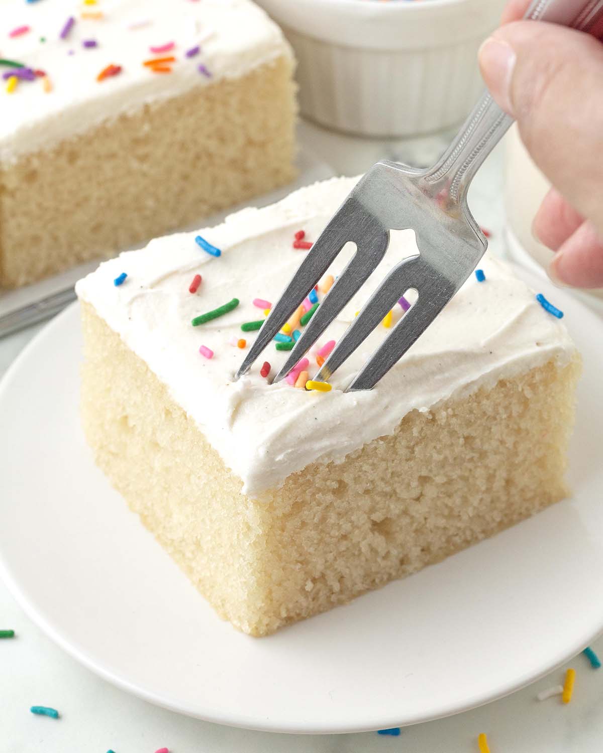A fork digging into a square of frosted vegan vanilla sheet cake.