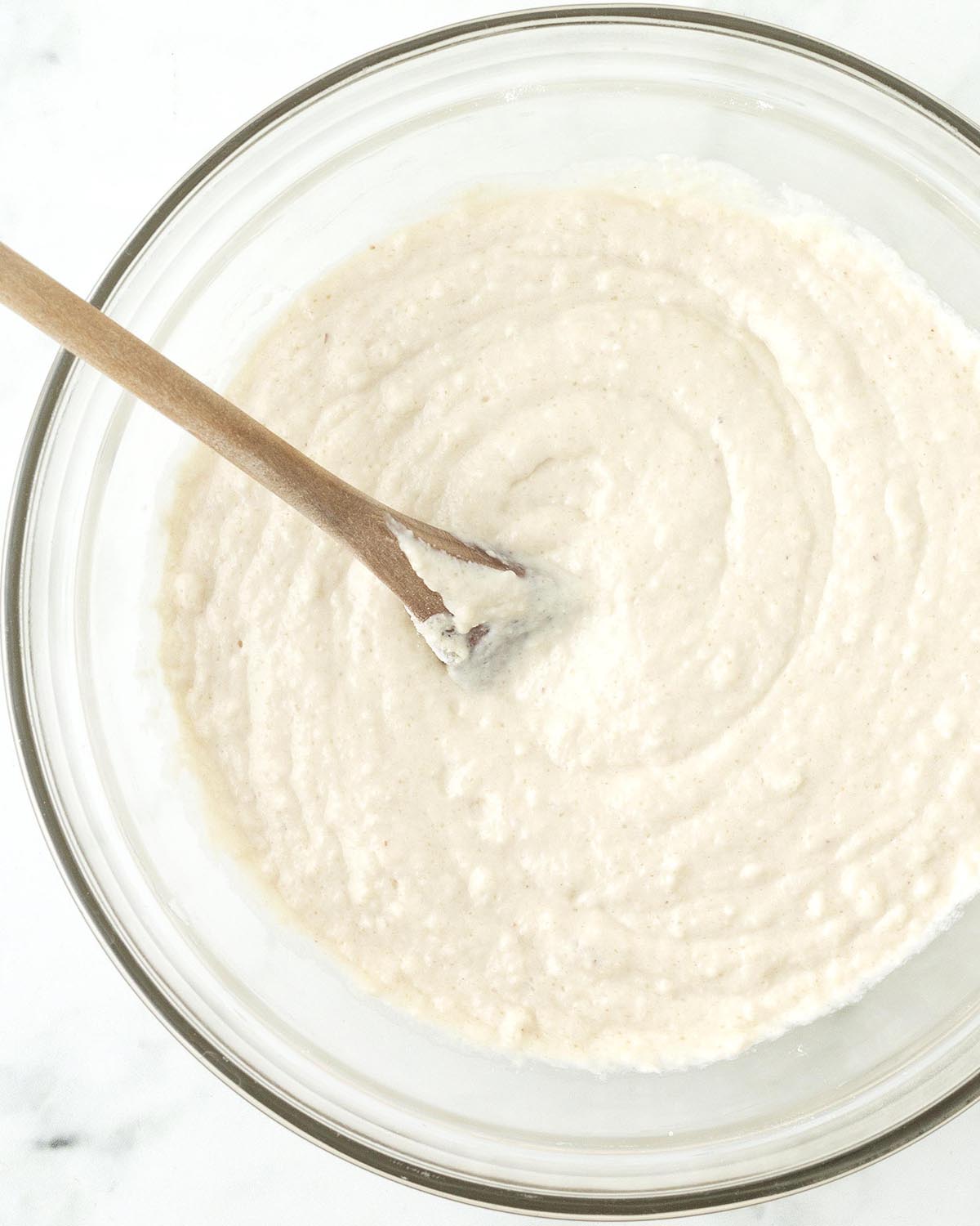 A bowl of vegan almond flour pancake batter, there is a wooden spoon in the bowl.