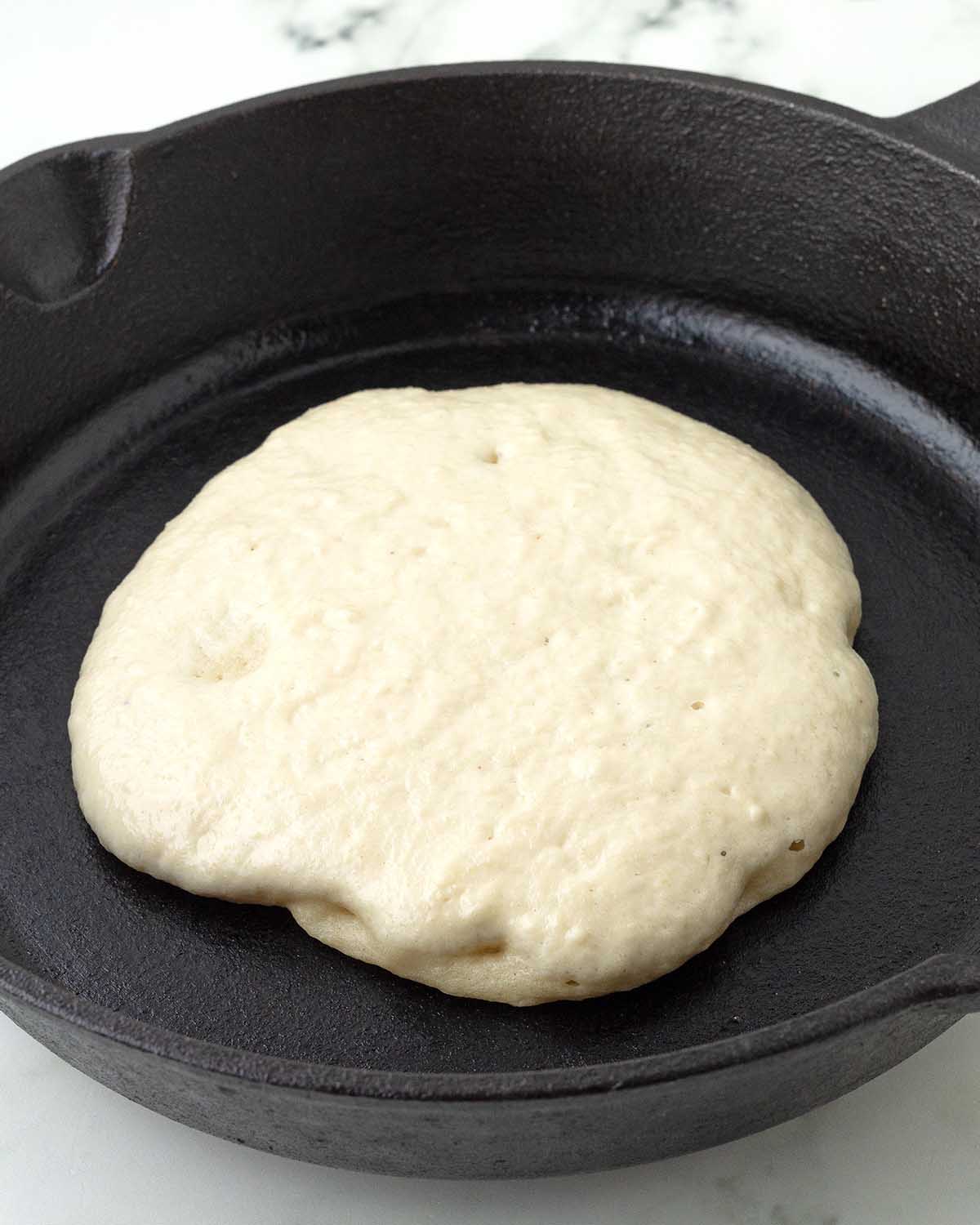 A vegan almond flour pancake cooking in a cast iron skillet just before being flipped.