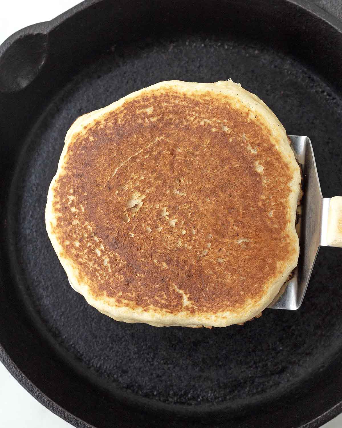A spatula holding up an almond flour pancake over a skillet.