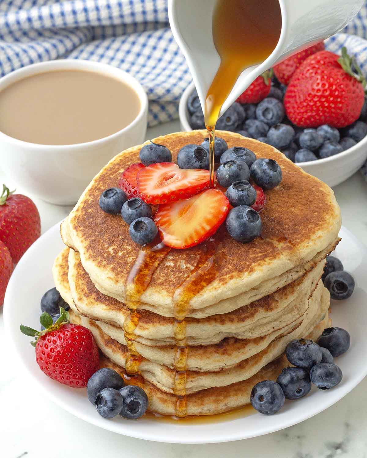 Maple syrup being poured from a carafe onto a stack of vegan almond flour pancakes.