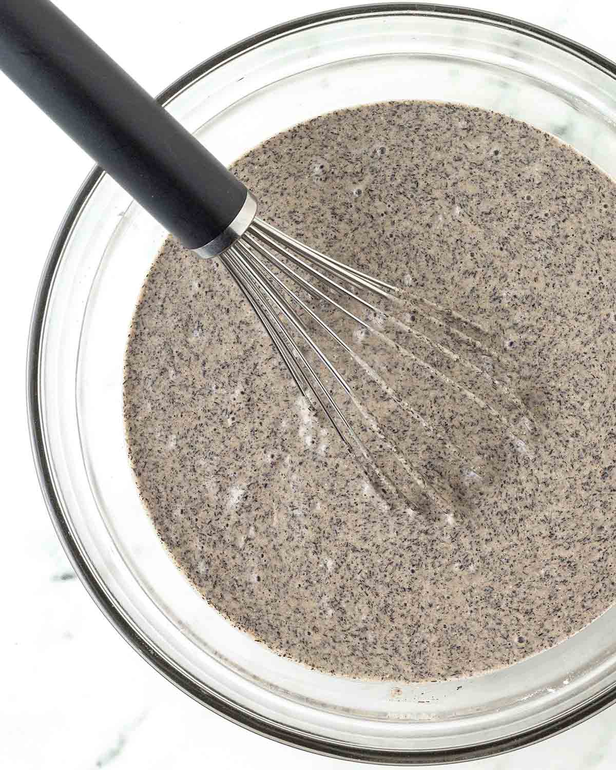 Vegan buckwheat waffle batter in a bowl with a whisk.
