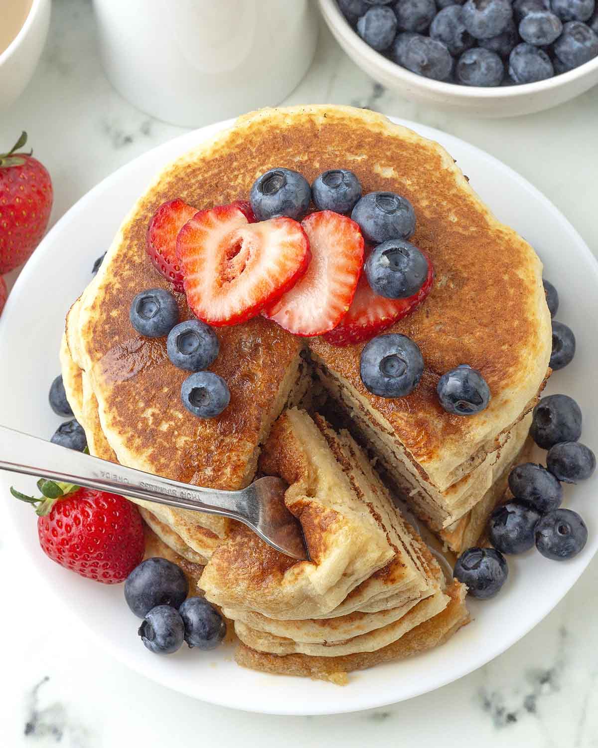 An overhead image showing a stack of pancakes, a wedge of the stack has been cut and on a fork.