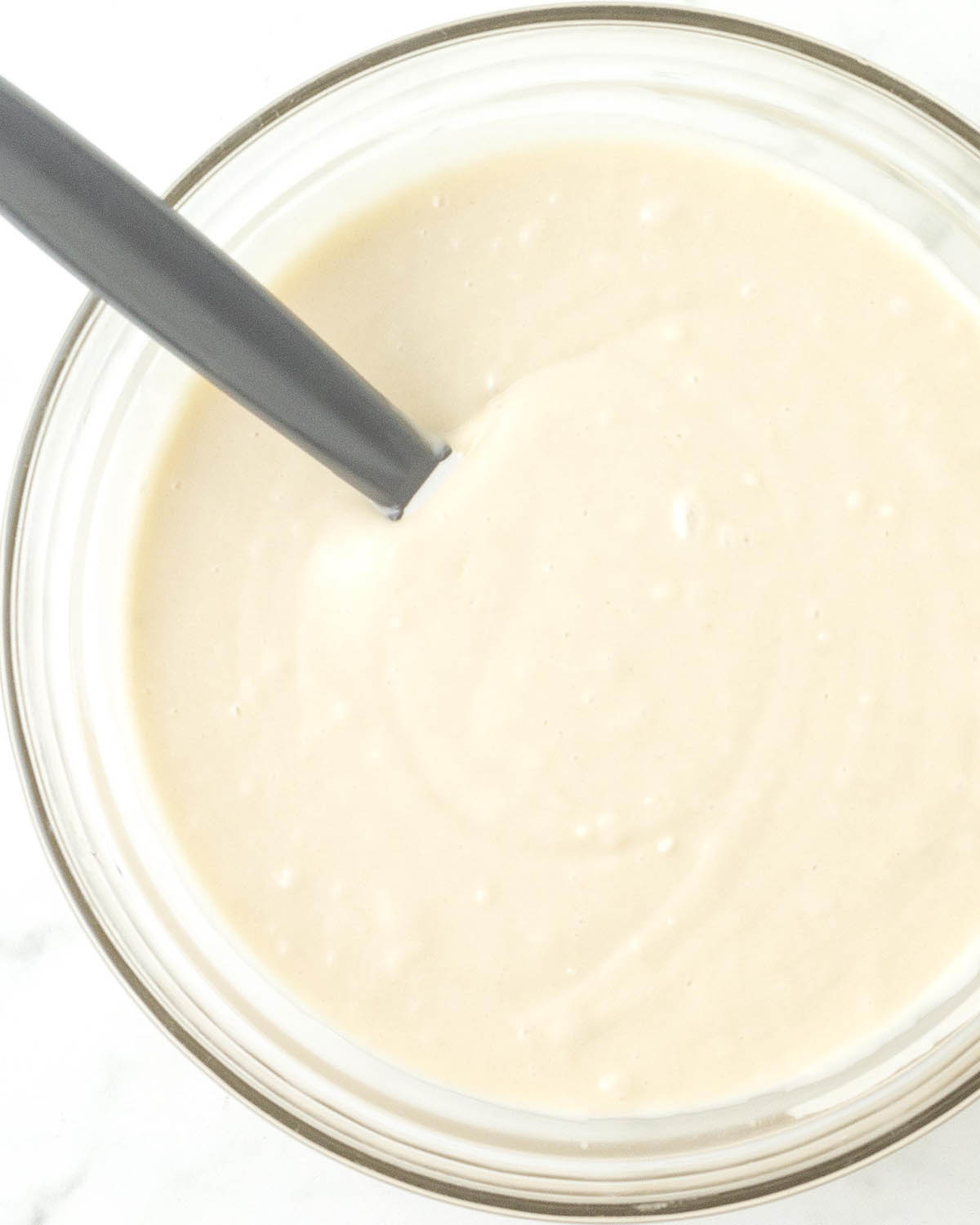 Mixed vanilla sheet cake batter in a glass bowl with a mixing spatula.
