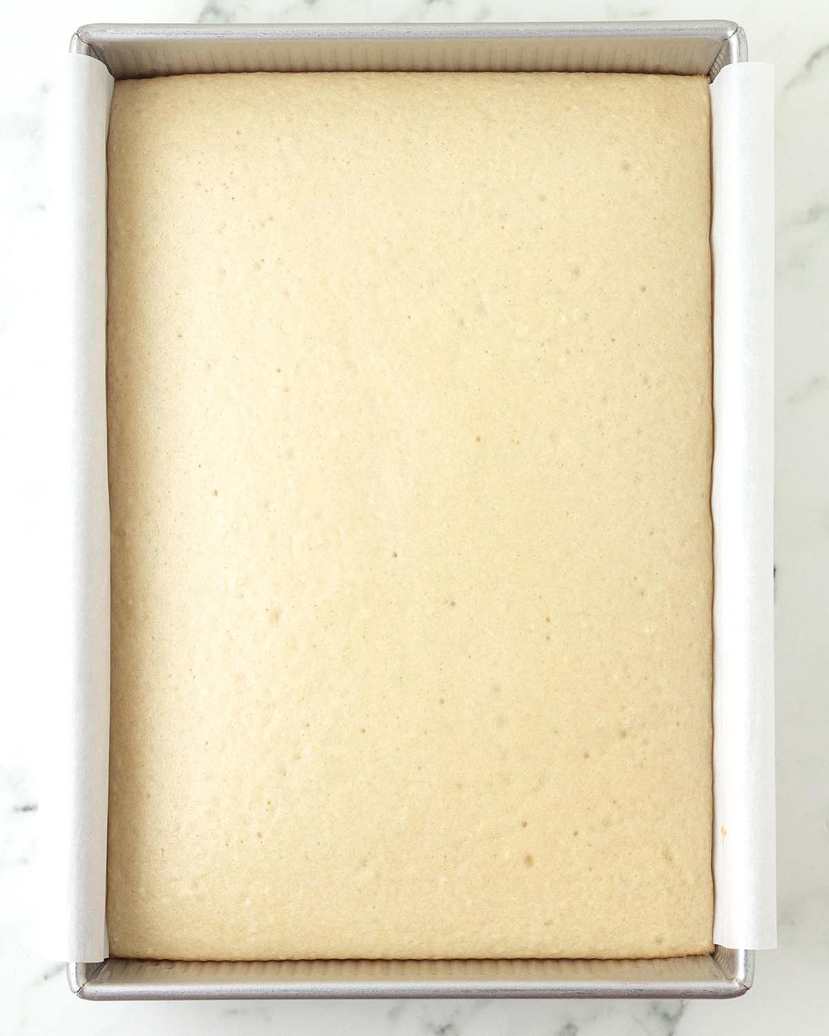 A freshly baked vegan vanilla sheet cake in a rectangle baking pan.