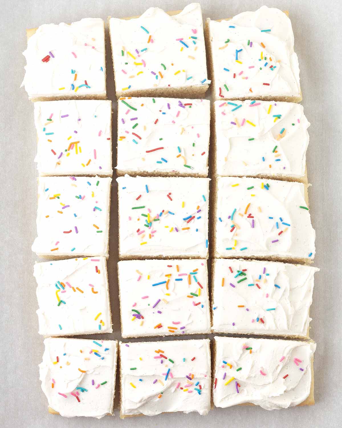 A frosted vegan vanilla sheet cake sliced into fifteen squares.