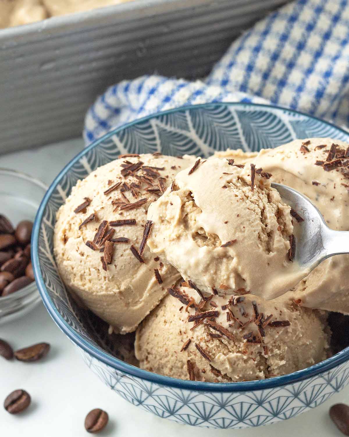 A spoonful of vegan coffee ice cream being held over a bowl of the same ice cream.