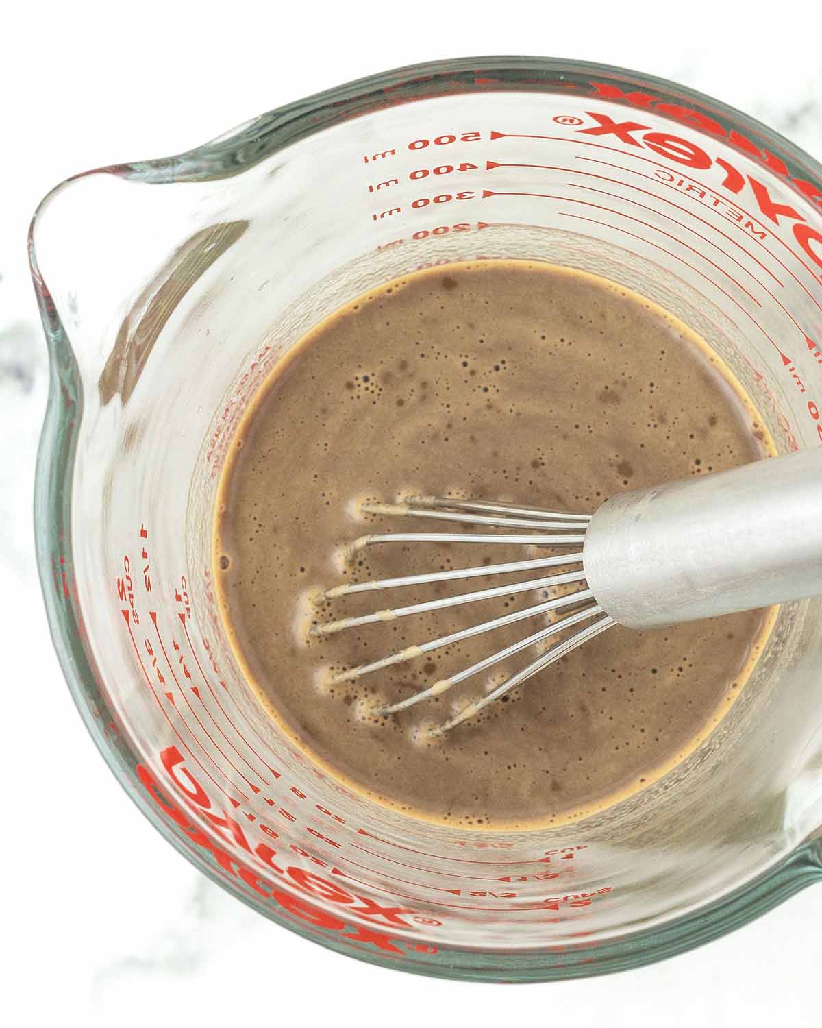 Instant coffee and milk whisked together in a measuring cup, a small whisk sits in the cup.